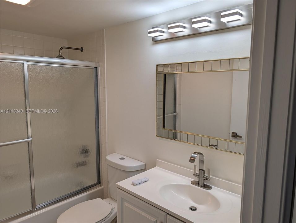 Bathroom featuring a vanity with integrated sink, brushed metal faucet, framed mirror with segmented detailing, four-light vanity fixture, and a tub with a sliding glass enclosure
