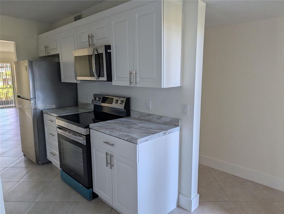 Kitchen featuring white shaker-style cabinetry, stainless steel appliances, stone-patterned countertops, and tile flooring