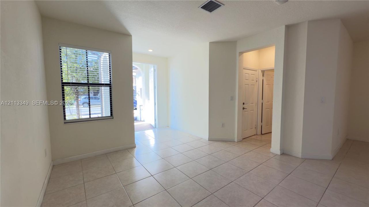 Neutral interior space featuring large-format ceramic tile flooring, a multi-pane window with dark frames, and two sets of interior paneled doors