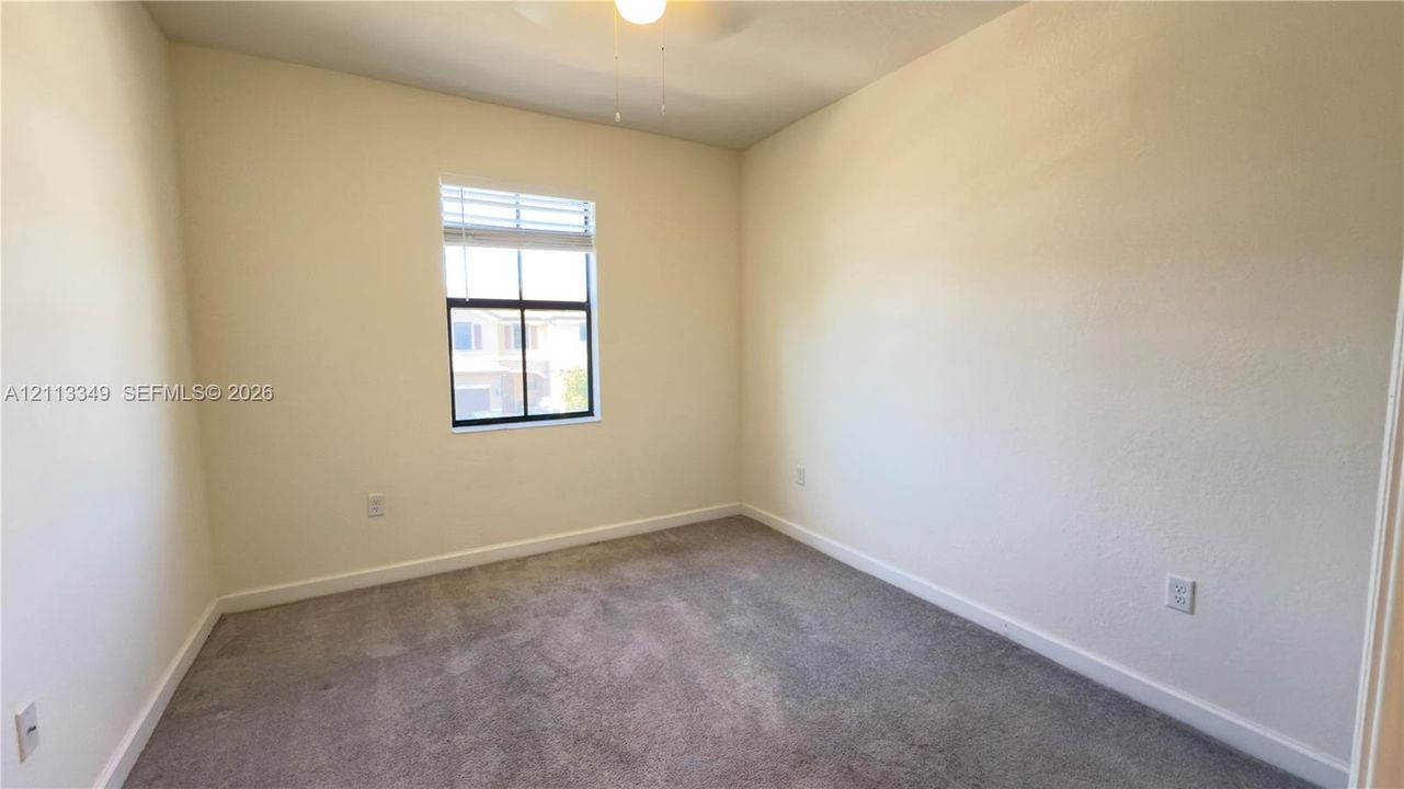 Neutral wall tones, carpeted flooring, single-pane window with blinds, and ceiling fan fixture