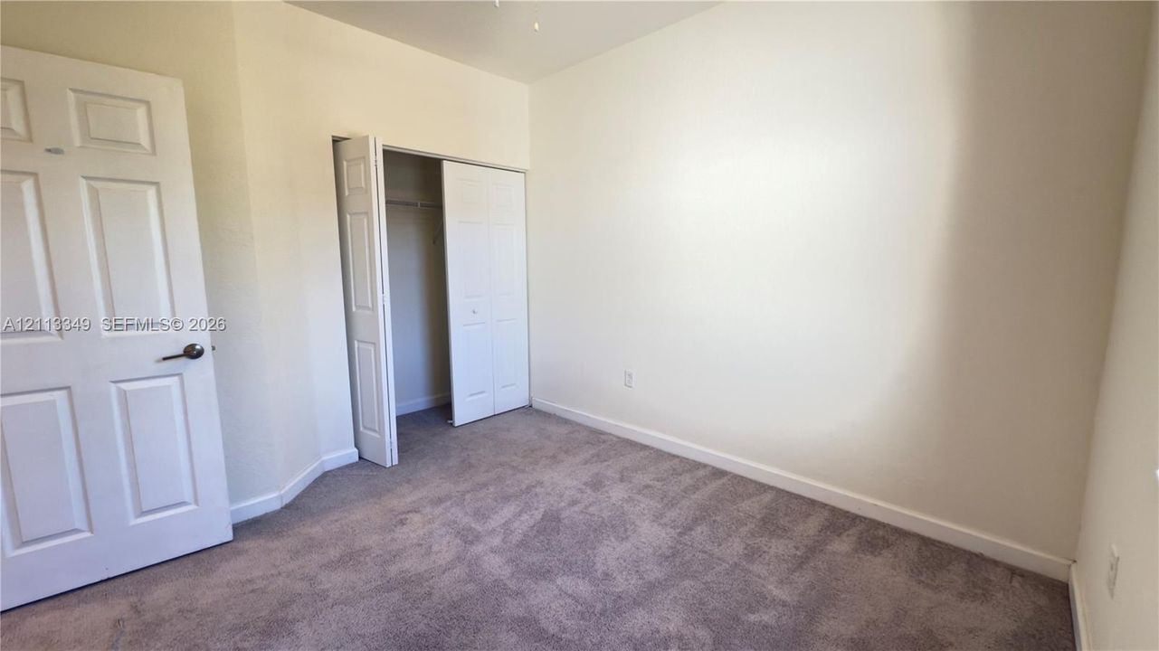 Neutral-toned interior space featuring neutral wall-to-wall carpeting, a six-panel interior door, and a reach-in closet with double-panel doors