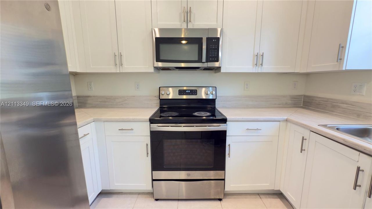 Kitchen featuring white shaker-style cabinetry, stainless steel appliances, neutral countertops, and coordinating backsplash