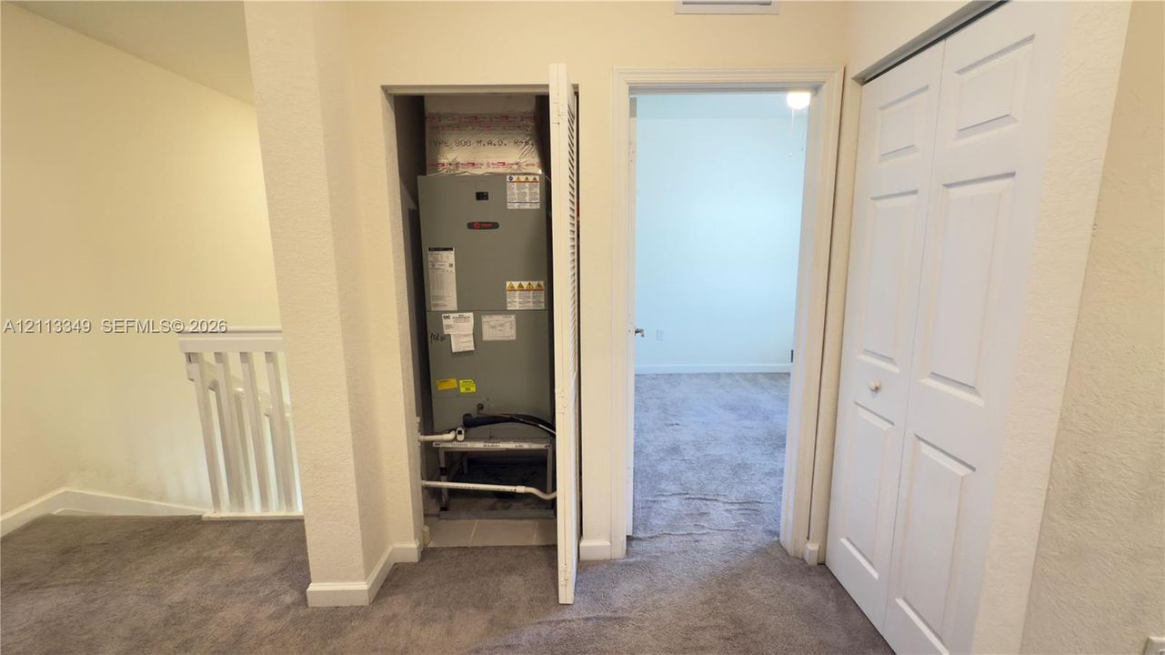 Utility closet featuring an HVAC unit with louvered door access, white-paneled closet doors, and wall-to-wall carpet