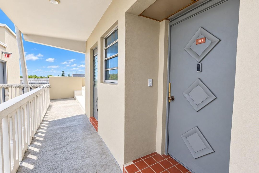 Covered exterior walkway featuring a concrete floor, diamond-accented door, terracotta tile entryway, and protective balustrade