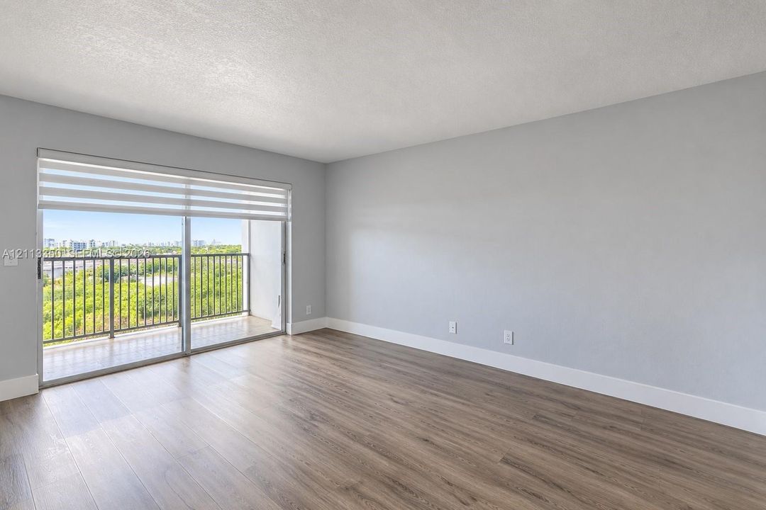 Living space featuring wood-finish flooring, neutral wall paint, and sliding glass doors with retractable shades opening to a balcony with metal railings