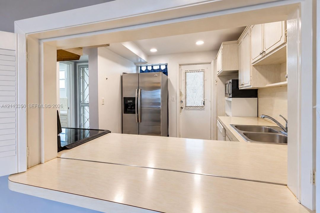 Kitchen featuring a pass-through counter, stainless steel refrigerator, double basin sink, and white cabinetry