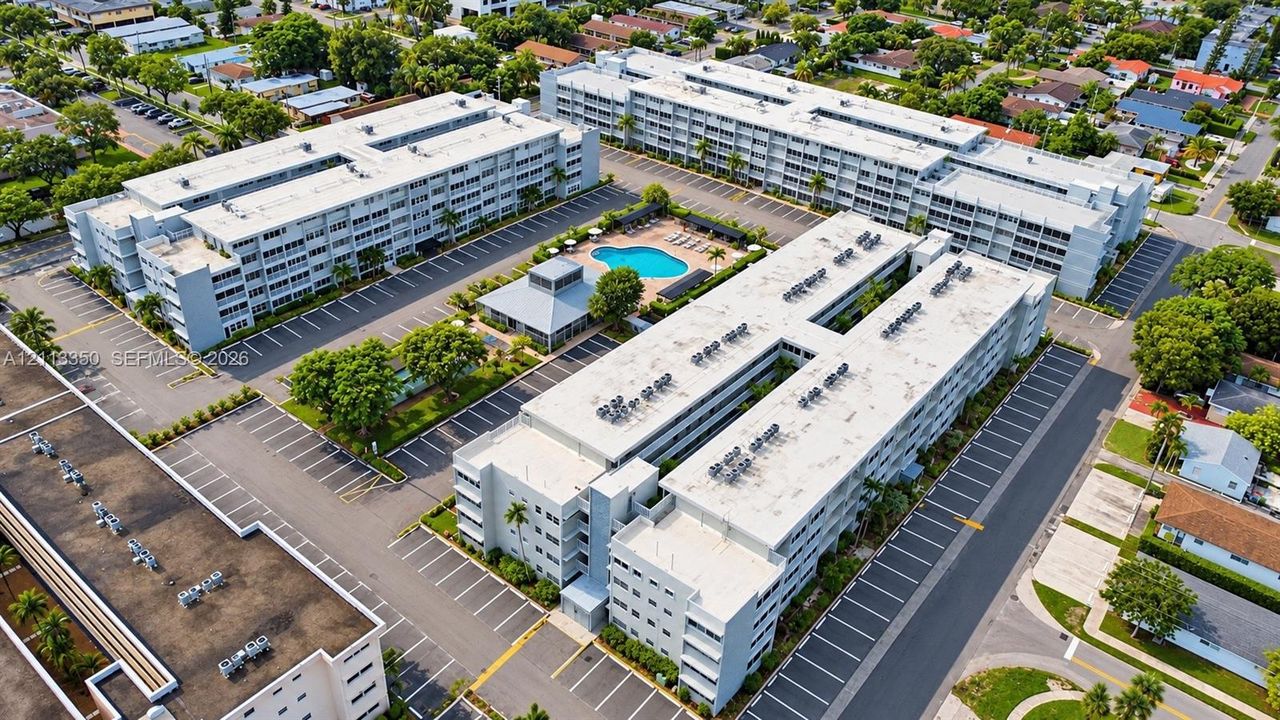 Aerial perspective of a multi-story residential complex featuring paved surface parking, an outdoor swimming pool, and a dedicated clubhouse structure