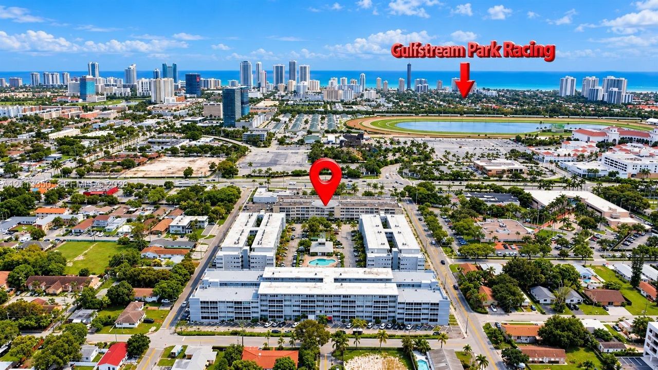 Aerial perspective of a multi-story residential complex featuring a central outdoor swimming pool and perimeter surface parking