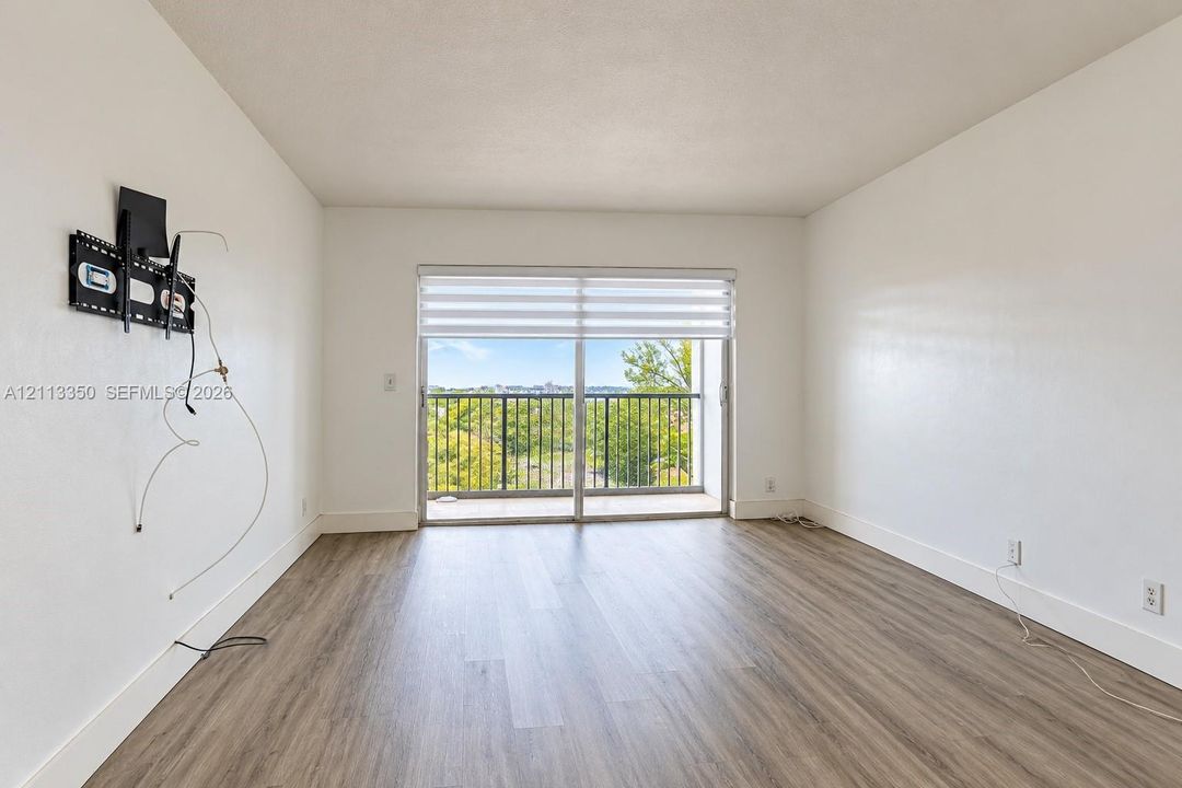 Wood-finish flooring, white walls, sliding glass door with dual-tone roller shade, and metal-railing balcony
