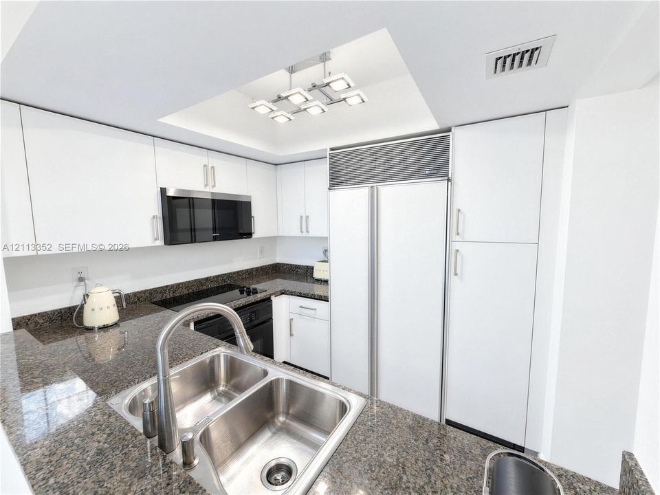 Kitchen featuring white flat-panel cabinetry, stone countertops, stainless steel dual-basin undermount sink, built-in panel-ready refrigerator, and integrated cooktop