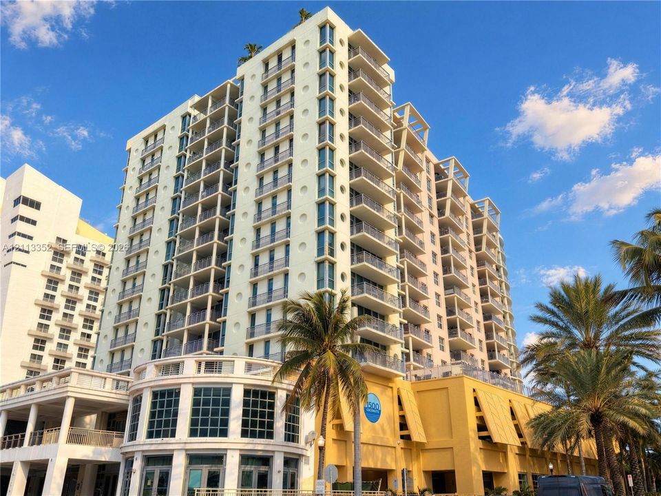 High-rise exterior featuring stacked balconies, decorative circular windows, multi-story glass facade, and structured parking podium