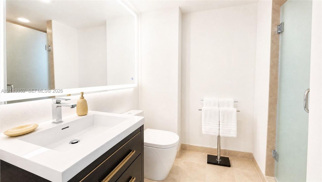 Bathroom featuring a dark wood-finish vanity with a white countertop and rectangular undermount sink, large wall-mounted mirror with integrated backlighting, dual-handle chrome faucet, and a glass-enclosed shower