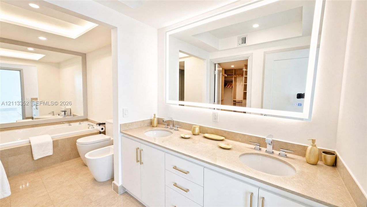 Dual-vanity cabinet with stone-finish countertops, undermount sinks, wall-to-wall LED-backlit mirror, built-in soaking tub, and tile flooring