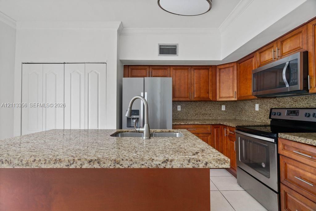 Kitchen featuring custom wood cabinetry, stone countertops, an island with an integrated stainless steel undermount sink, and stainless steel appliances