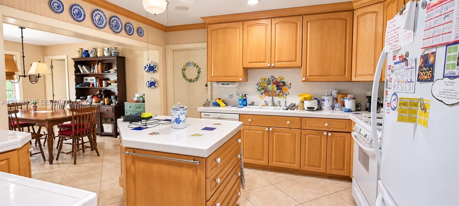Kitchen featuring natural wood cabinetry, a central island with a tiled countertop, ceramic tile flooring, and integrated white appliances