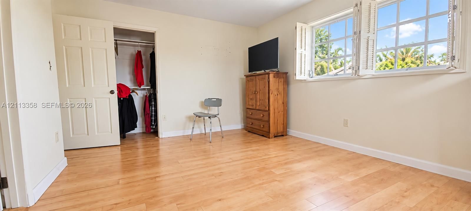 Room featuring wood-finish flooring, multi-pane windows with operable shutters, and a built-in closet with six-panel door