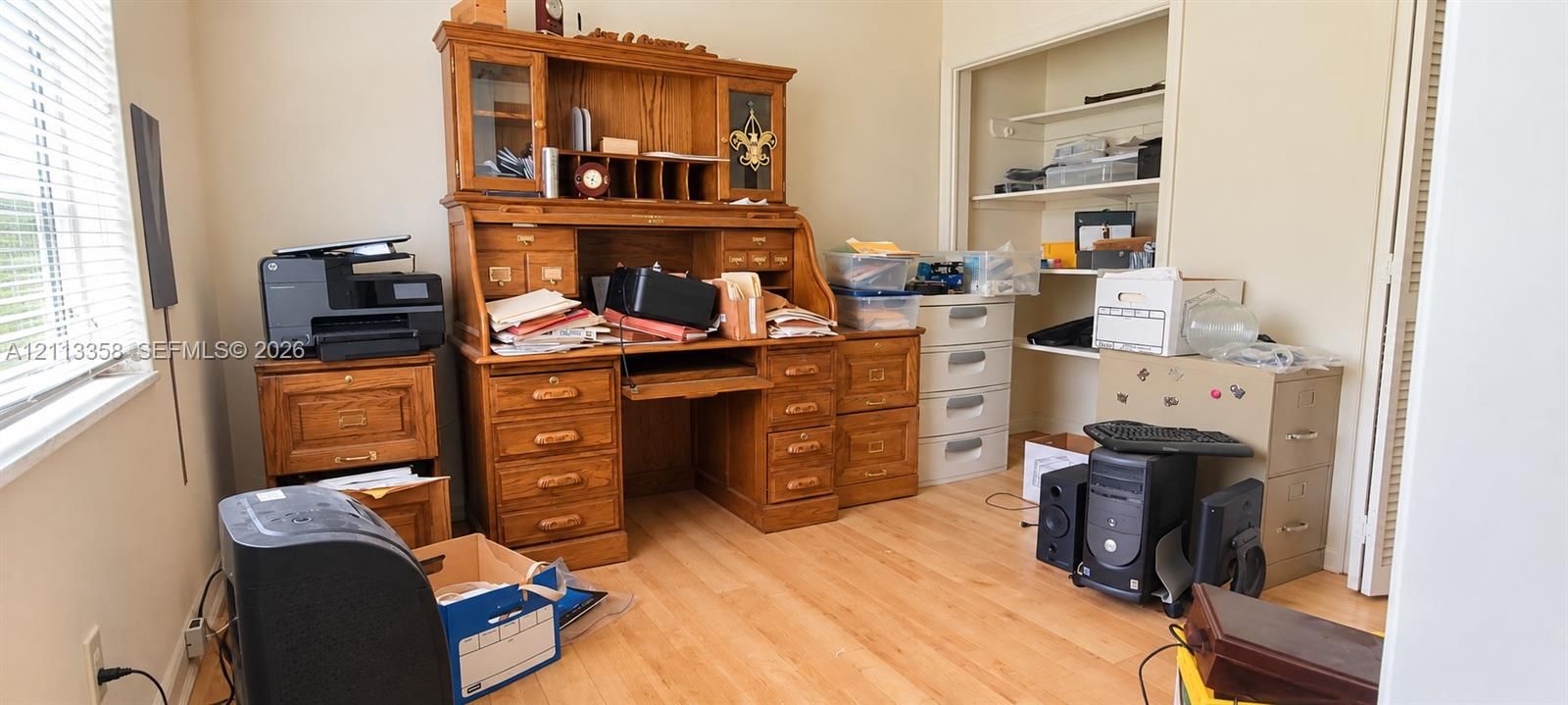Room featuring wood-finish flooring, white walls, horizontal window blinds, and a built-in closet with shelving