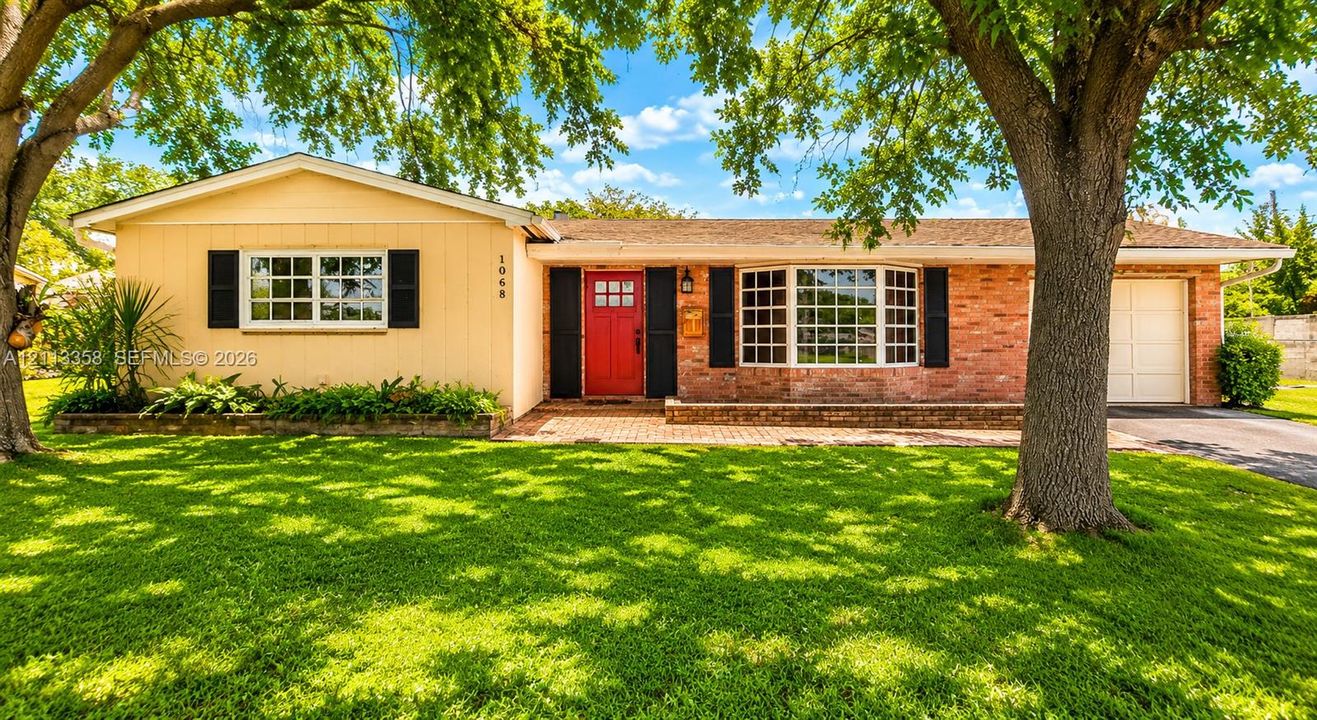 Single-story exterior featuring a brick and panel facade, bay window, red entry door with decorative glass, and attached garage