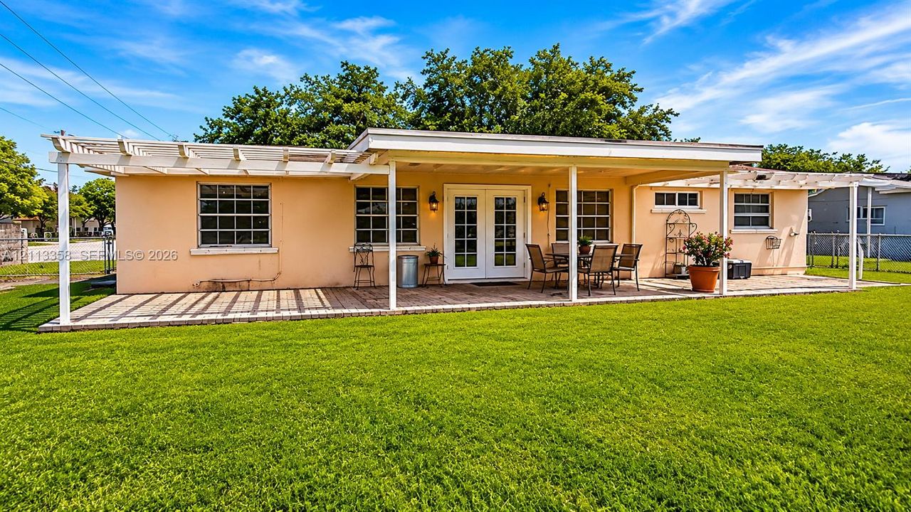 Rear exterior featuring an expansive lawn, a covered patio with a paved surface, and dual pergola structures