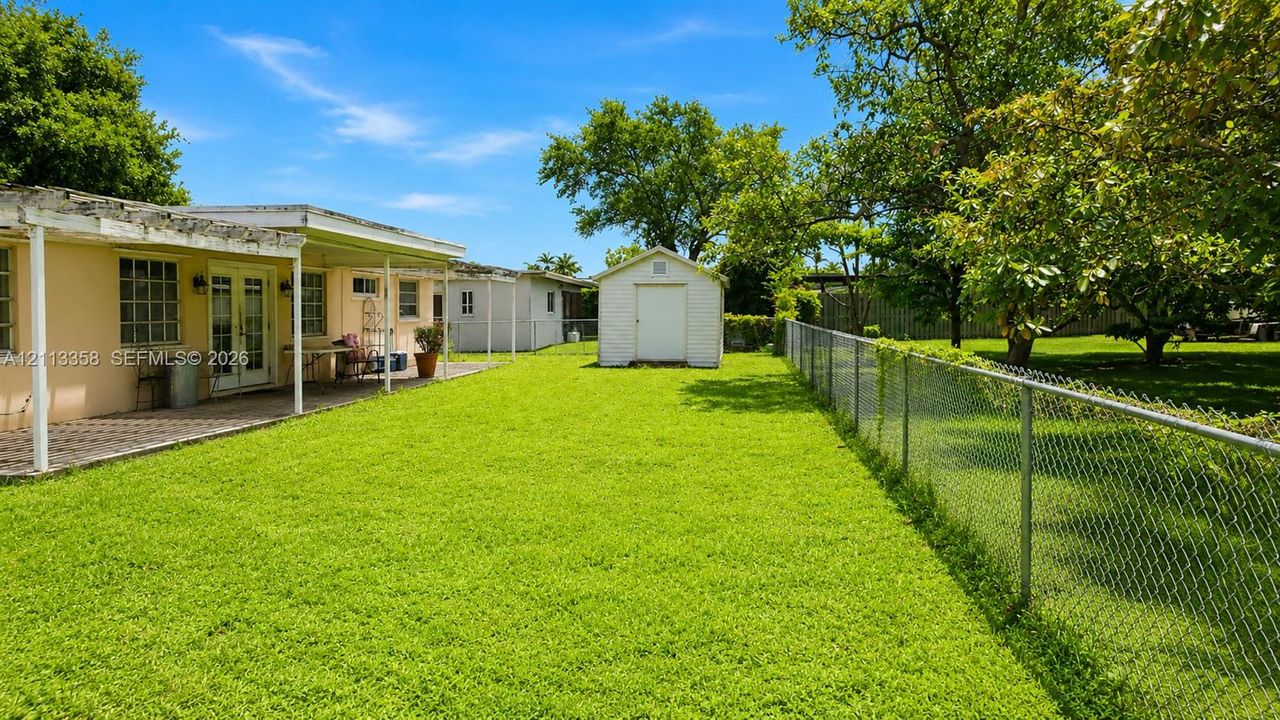 Expansive backyard featuring a covered patio, detached storage shed, chain-link fencing, and mature trees