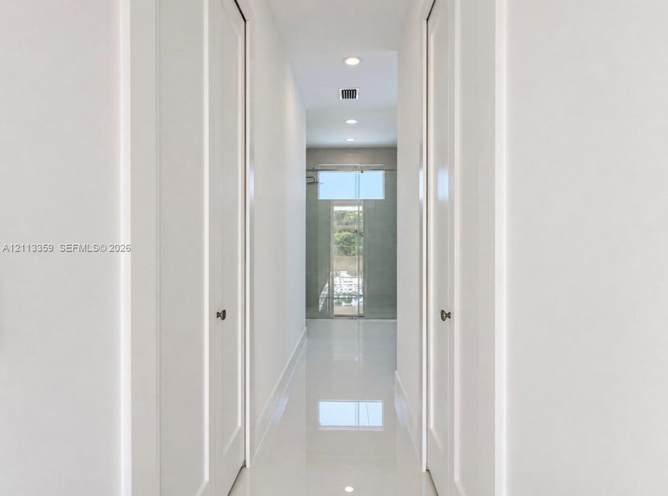 Hallway featuring high-gloss tile flooring, recessed ceiling lighting, and dual floor-to-ceiling closets with paneled doors