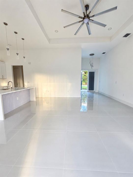 Open-concept interior featuring large-format tile flooring, tray ceilings, recessed lighting, multi-blade ceiling fan, and kitchen peninsula with vertical slat detailing