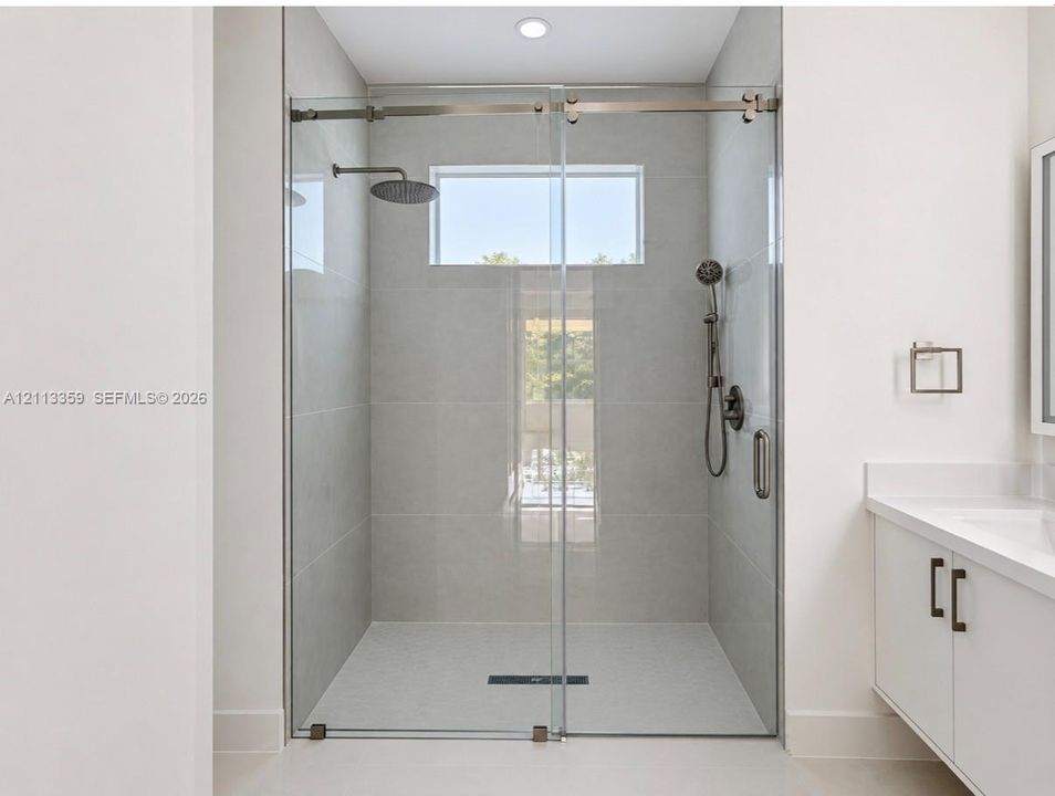 Walk-in shower featuring large-format tile surround, frameless glass sliding enclosure, rainfall showerhead, handheld sprayer, and transom window