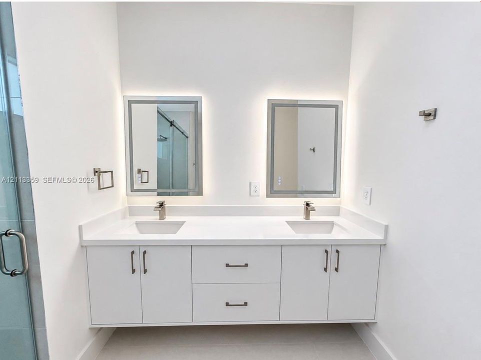 Floating double vanity featuring a white countertop with dual undermount sinks, satin-finish faucets, built-in lower cabinetry, and two rectangular LED-backlit mirrors