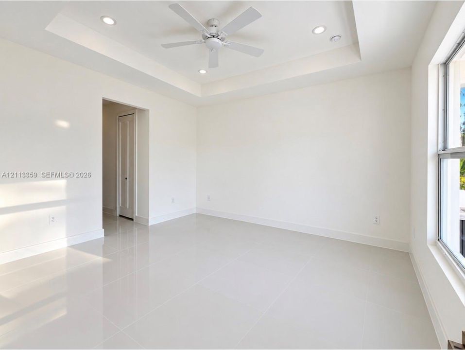 Tray ceiling with recessed lighting, white tile flooring, ceiling fan, and large windows
