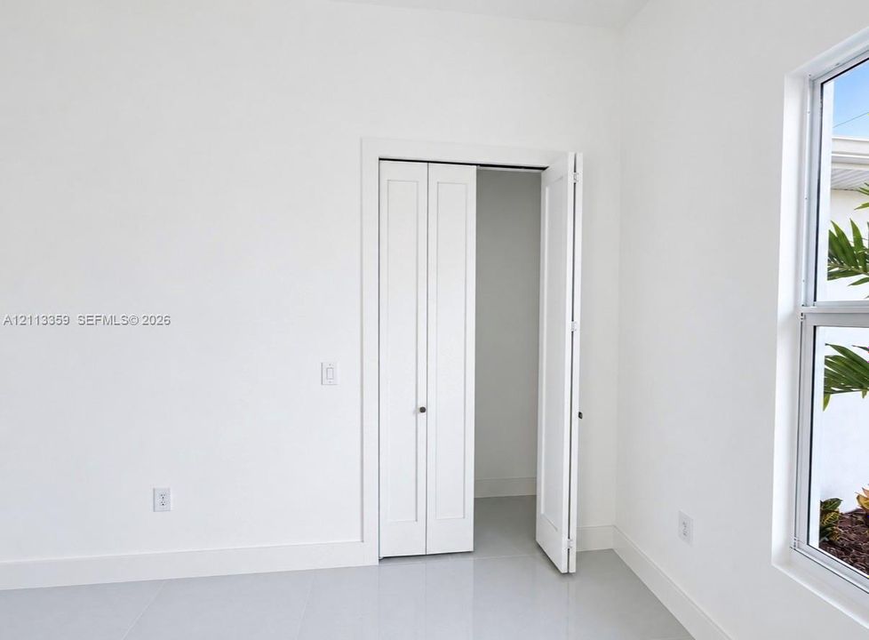 Neutral-toned tile flooring, white-finished walls, and a multi-panel bifold closet door