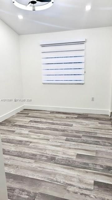 Room featuring wood-finish flooring, recessed lighting, a modern circular ceiling fixture, and dual-layer adjustable roller shades