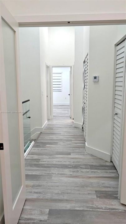 Hallway featuring wood-finish flooring, high ceilings, glass panel railing, and white louvered closet doors