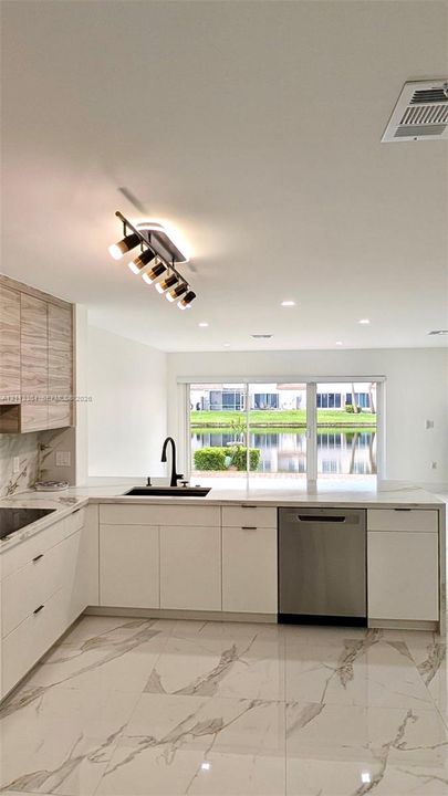 Kitchen featuring white flat-panel cabinetry, light-toned wood-finish upper cabinets, large-format veined tile flooring, a stainless steel dishwasher, and a multi-light track fixture
