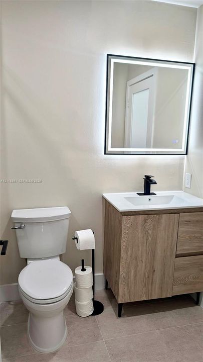 Vanity featuring a light wood-finish cabinet with white countertop, integrated rectangular sink, matte black faucet, and rectangular LED-backlit mirror