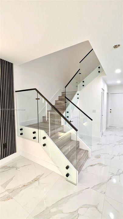 Staircase featuring wood-finish treads, frameless glass railings with black hardware, and vertical slat accent wall paneling over large-format tile flooring