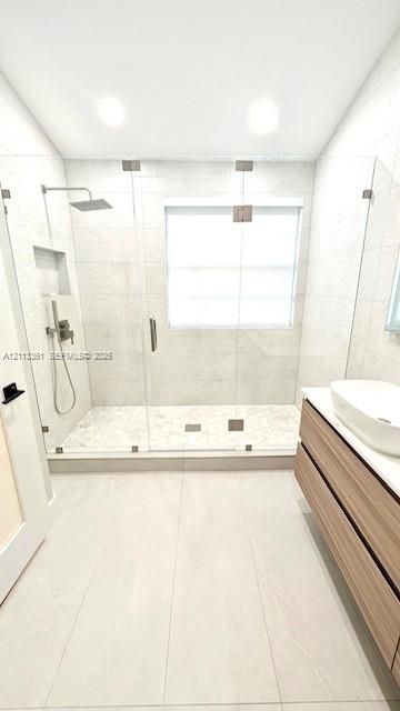Walk-in shower featuring a frameless glass enclosure, rainfall showerhead with a handheld sprayer, wall-integrated niche, and wood-finish floating vanity with a vessel sink