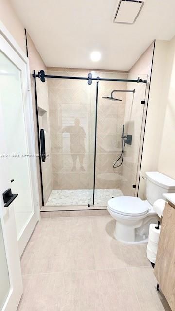 Walk-in shower featuring a sliding glass enclosure with matte black hardware, herringbone-patterned wall tile, pebble-style floor tiling, and a rainfall showerhead