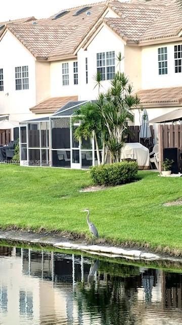 Two-story exterior featuring multi-pitched rooflines, a screened-in lanai, waterfront grass area, and mature landscaping