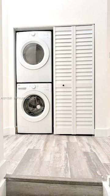 Stacked laundry unit with white louvered bifold closet doors and wood-finish flooring