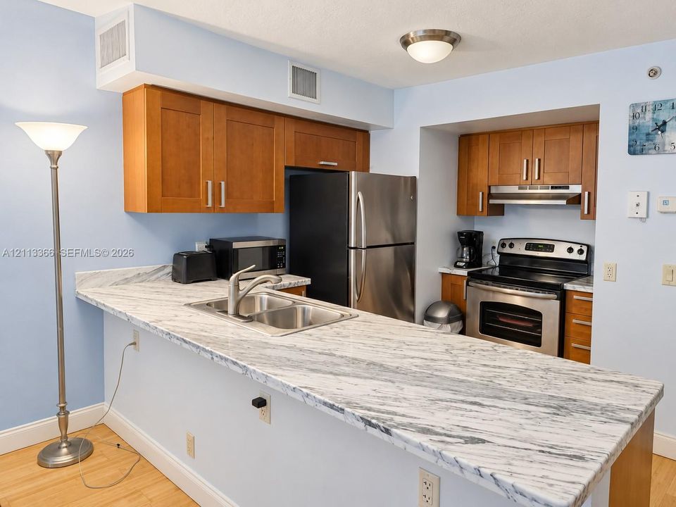 Kitchen featuring wood-finish cabinetry, stone-patterned countertops, a stainless steel double-basin sink, and integrated stainless steel appliances