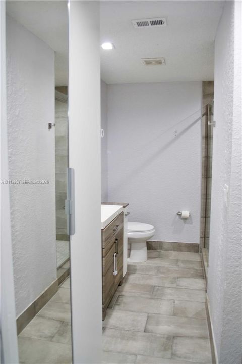Bathroom featuring wood-finish vanity cabinetry, a rectangular sink, neutral large-format tile flooring, a glass-enclosed shower, and recessed ceiling lighting
