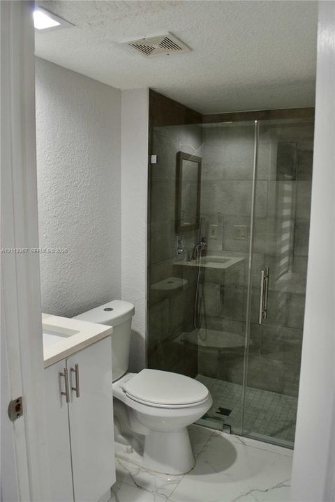 Bathroom featuring large-format tile flooring, white cabinetry with a light-toned countertop, and a walk-in shower enclosed by a glass door with tiled wall surrounds