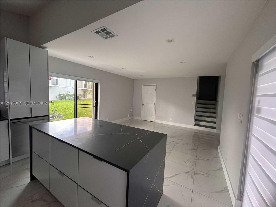 Kitchen featuring a waterfall-edge island with stone-finish countertop, white flat-panel cabinetry, large-format tile flooring, and sliding glass doors