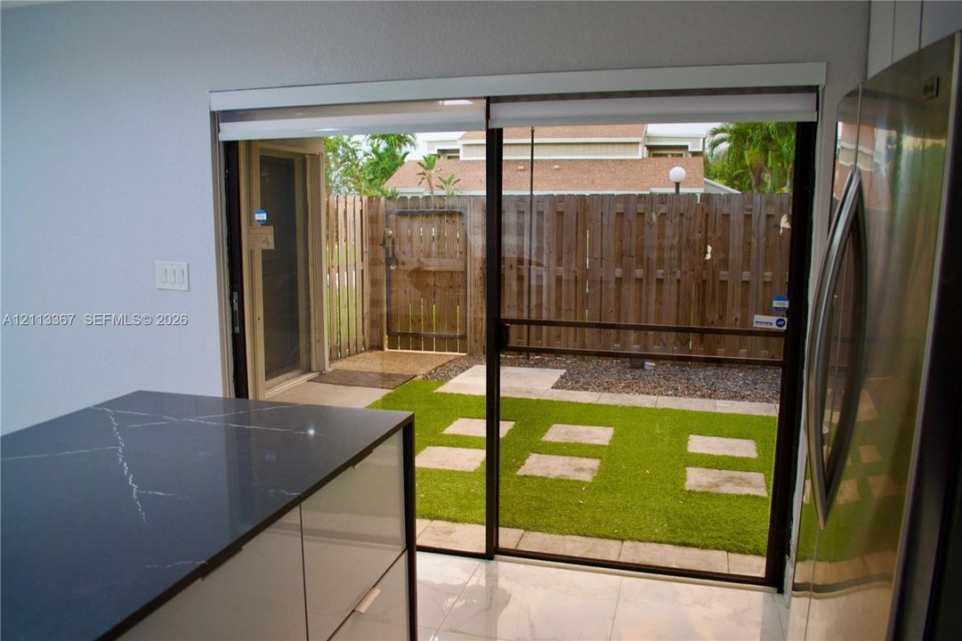Sliding glass door opening to a private patio featuring synthetic turf, paver stepping stones, and wood fencing