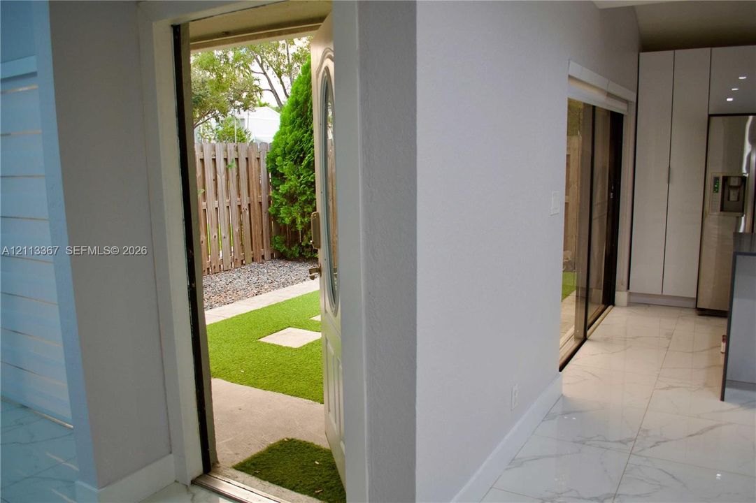 Large-format tile flooring, white floor-to-ceiling cabinetry, sliding glass door, and exterior access to a fenced courtyard featuring synthetic turf and stone pavers