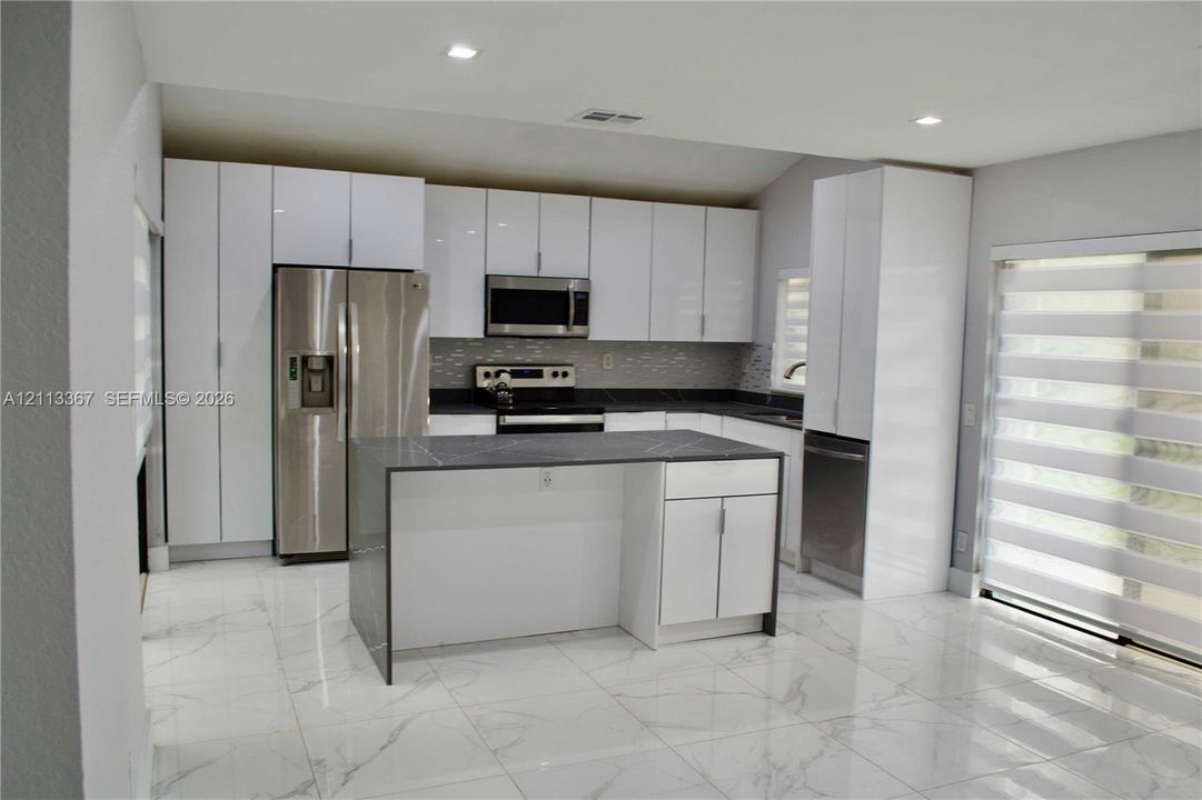 Kitchen featuring high-gloss white cabinetry, a center island with a dark stone countertop, stainless steel appliances, and large-format porcelain tile flooring