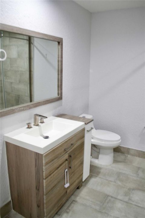 Wood-finish vanity cabinet, integrated rectangular sink, wall-mounted mirror with a coordinating wood-finish frame, and tile flooring