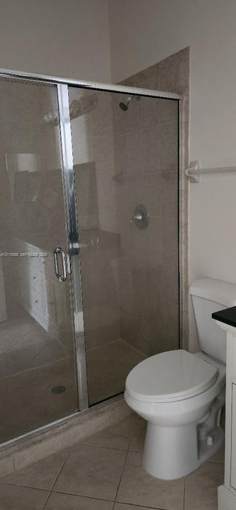 Walk-in shower with a glass enclosure, tiled surround, and chrome fixtures, paired with a white porcelain toilet and tile flooring