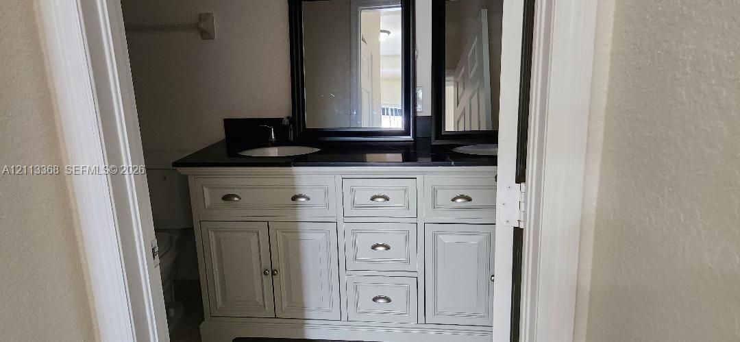 White cabinetry vanity featuring a dark countertop, dual undermount sinks, central drawer bank, and two framed wall mirrors