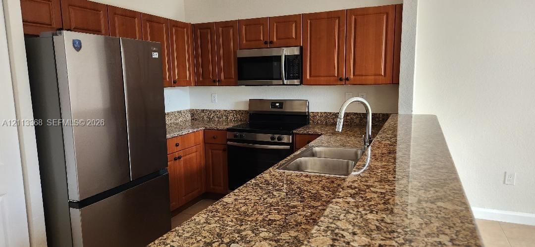 Kitchen featuring raised-panel wood cabinetry, stone countertops, stainless steel appliances, and a dual-basin sink with a high-arch faucet